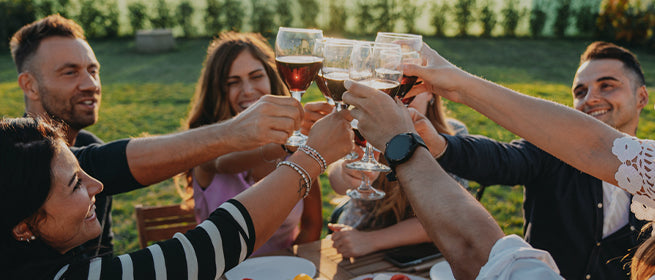 Benvenuti da Vinoreale. Le persone sono sedute all'aperto e brindano insieme con i calici di vino.