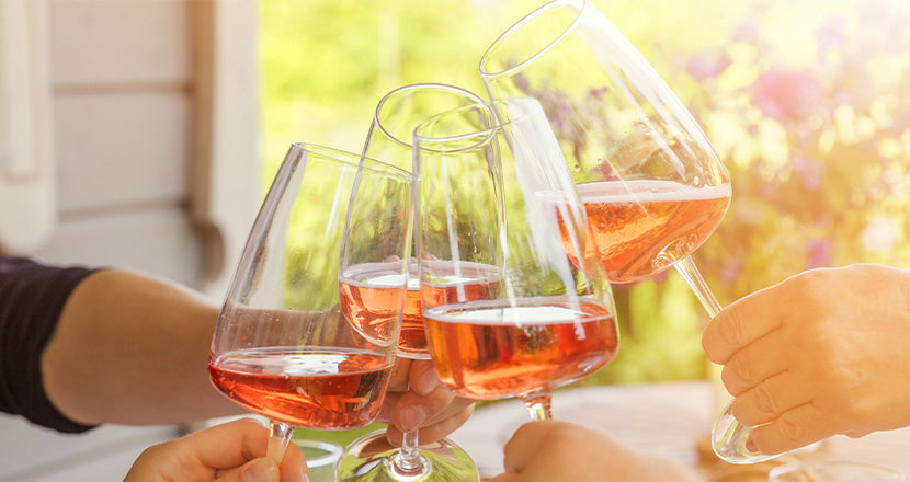 Quattro persone brindano con bicchieri di vino rosato sotto il caldo sole pomeridiano.