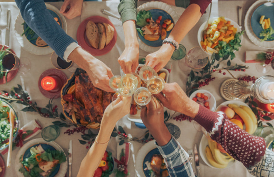 Vista dall’alto di una tavola invernale apparecchiata in modo festoso, dove più persone brindano con i bicchieri.